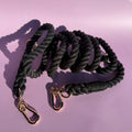 A 7ft black multi-use rope dog lead with gold-style clasps and rings, displayed against a purple background.