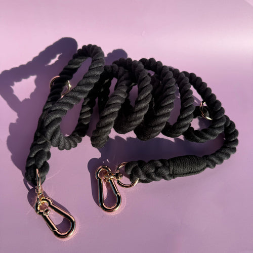 A 7ft black multi-use rope dog lead with gold-style clasps and rings, displayed against a purple background.