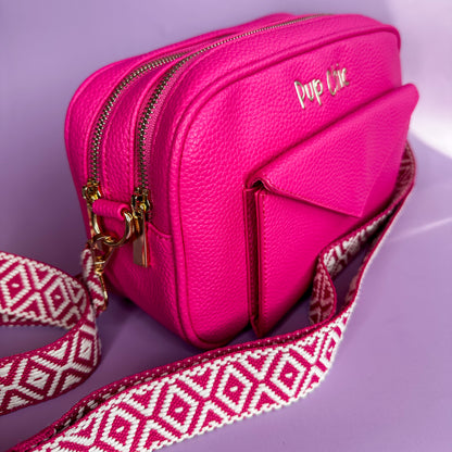 Pink handbag with a patterned strap on a purple background