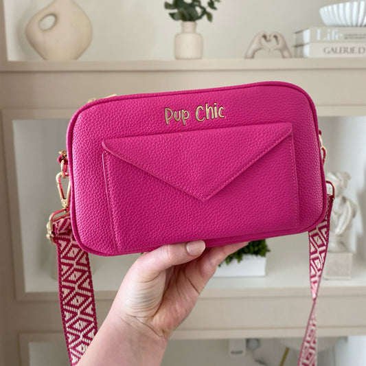 Pink crossbody bag with 'Pup Chic' branding held by a hand in a room setting.
