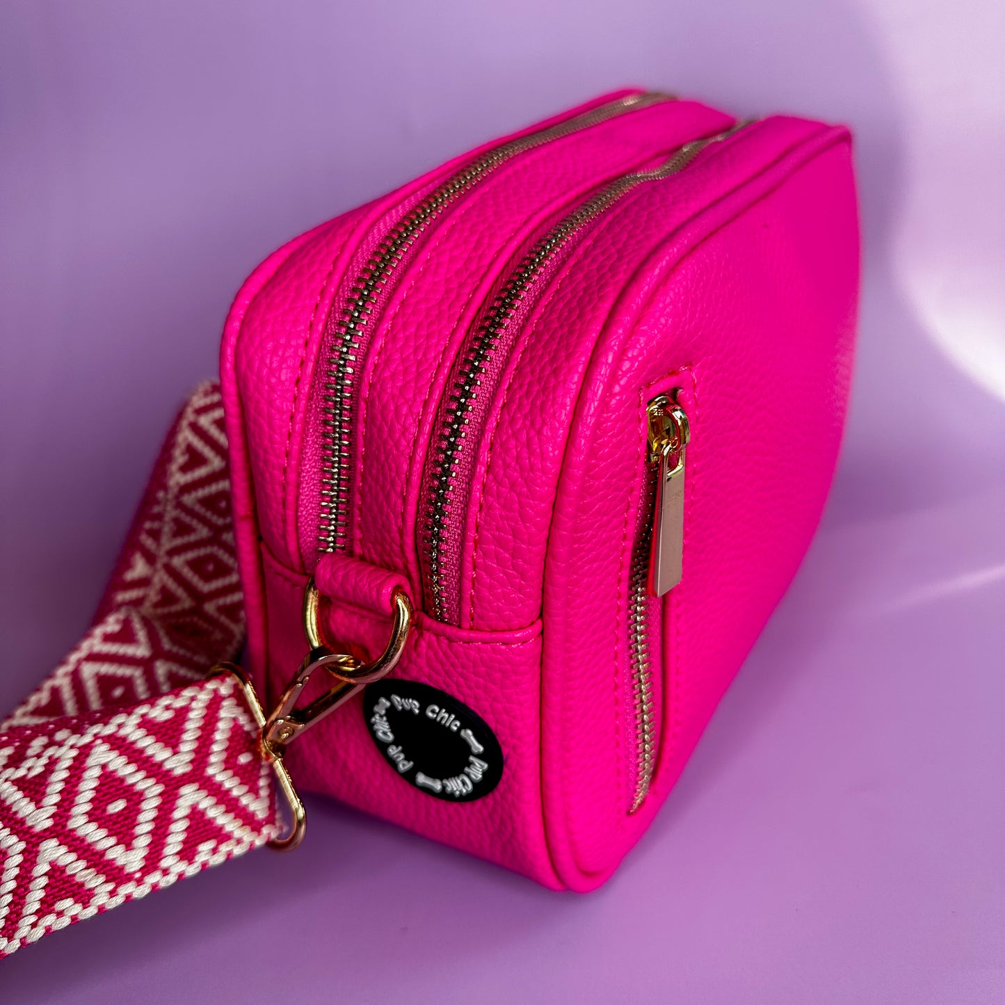 Pink crossbody dog walking bag with gold zippers and a poo bag dispense on a purple background
